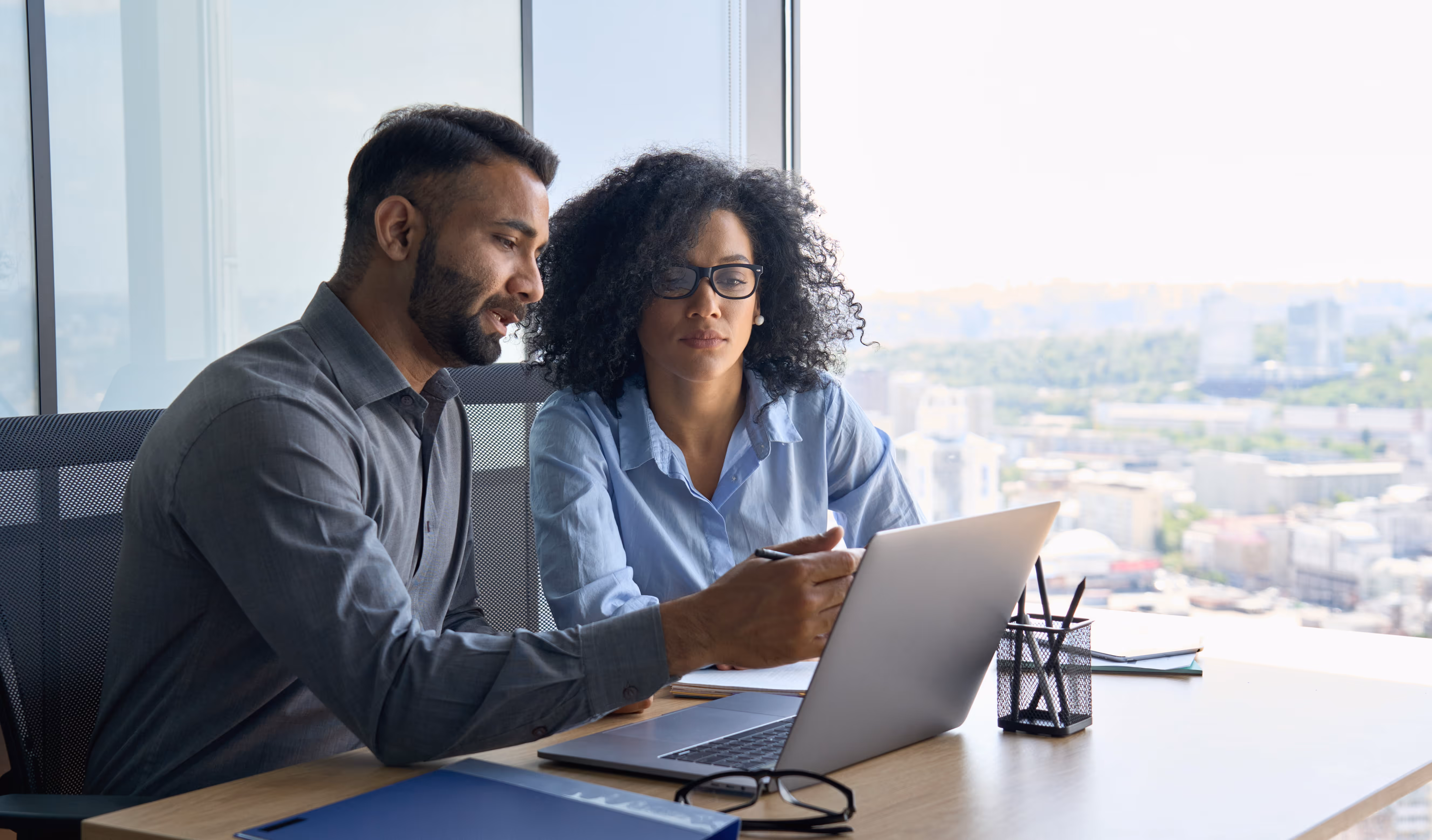 A male colleague shows teaches a female colleague on her laptop