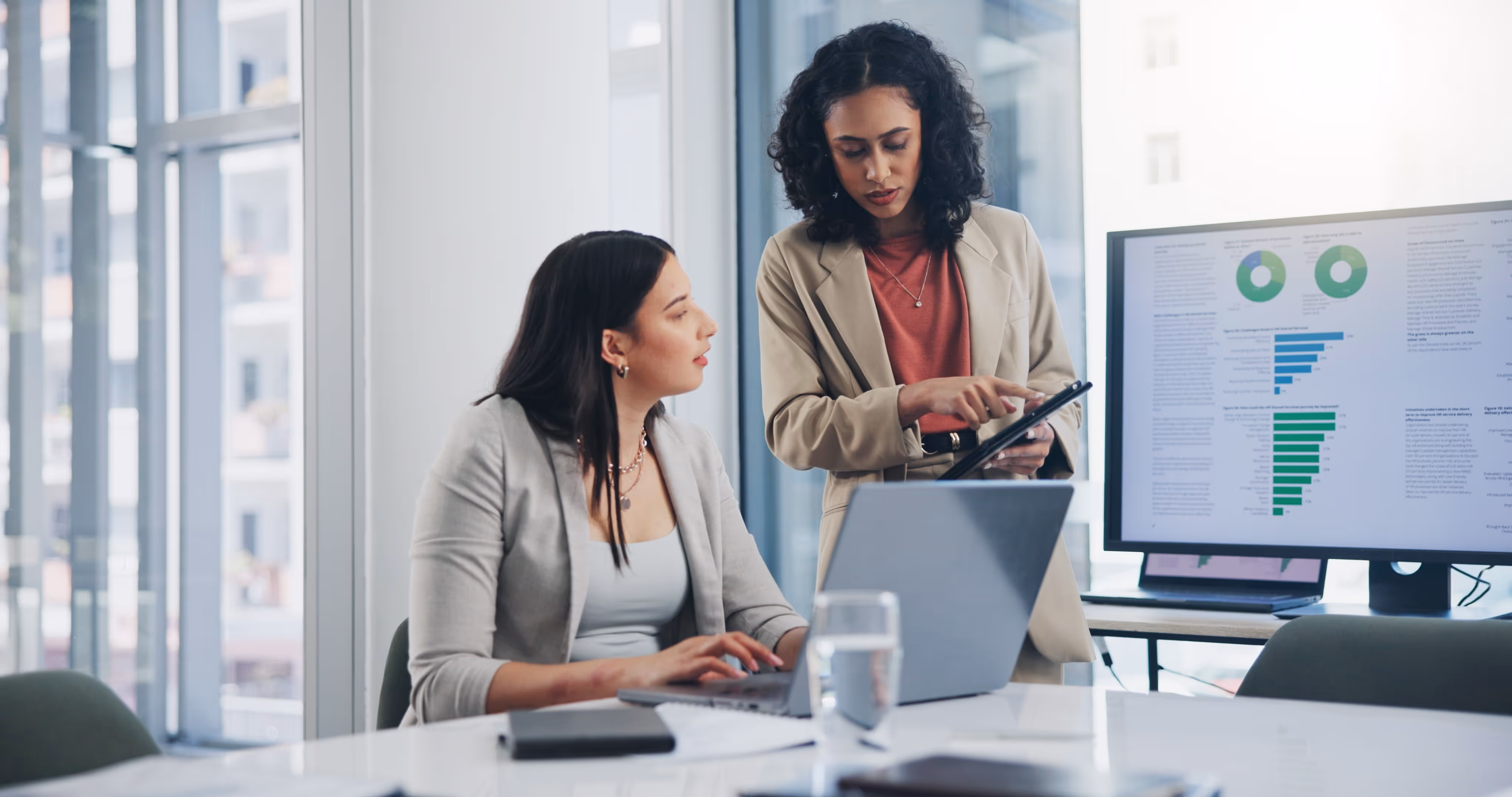 Two colleagues working together as one standing points to something on her tablet to the other.